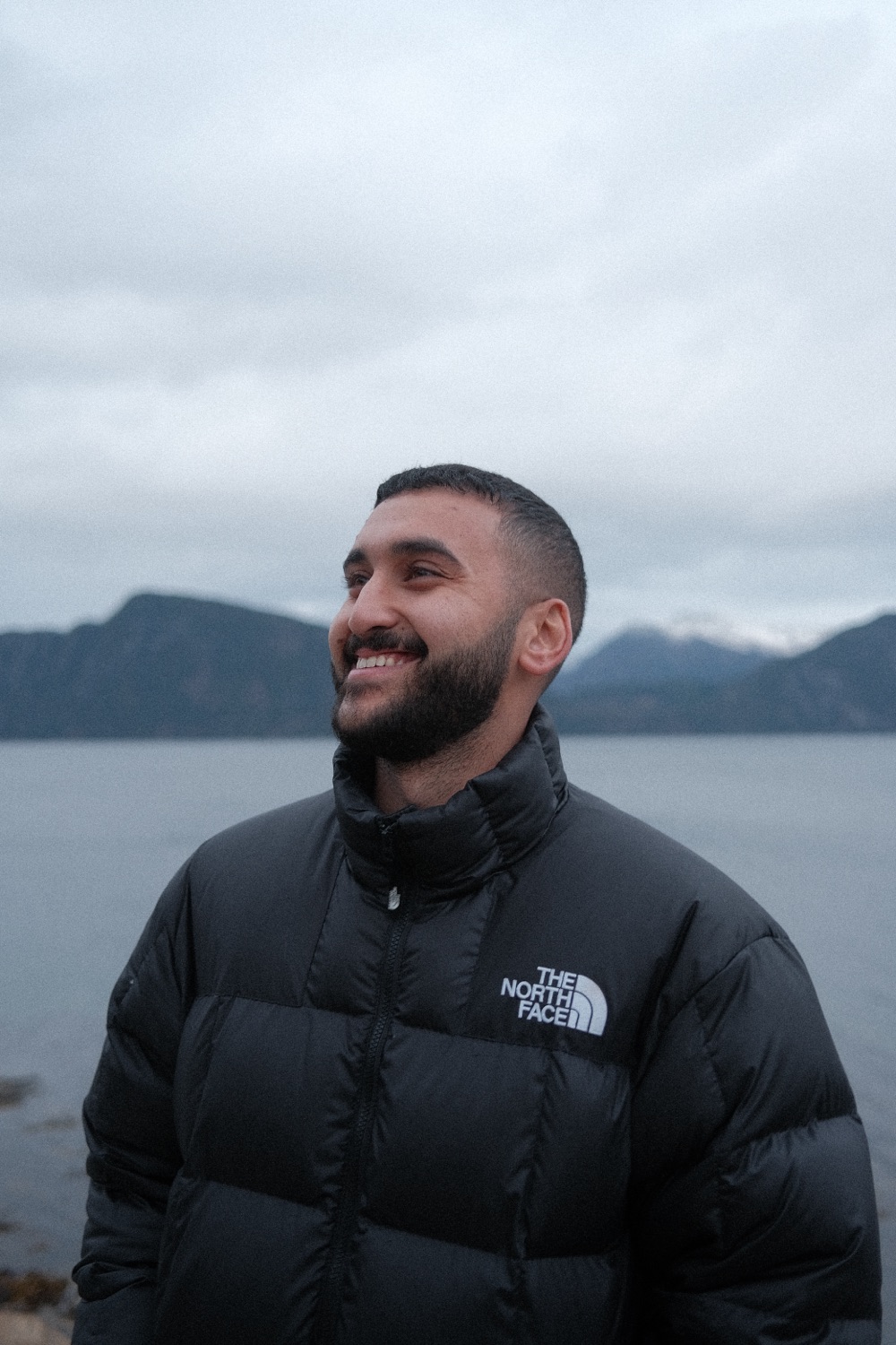 Abdalla Moussa smiling by a lake with mountains behind him